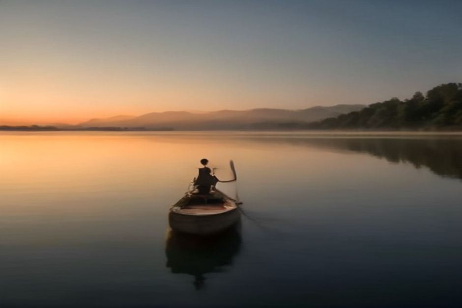 A rowing shell on calm water at dawn with mist rising, muted earth tones, a single rower stretching on the dock