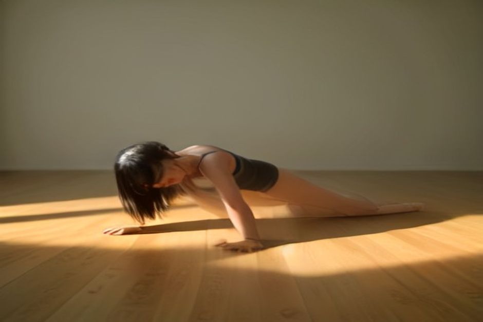A person holding a steady plank pose on a wooden floor in calm natural light