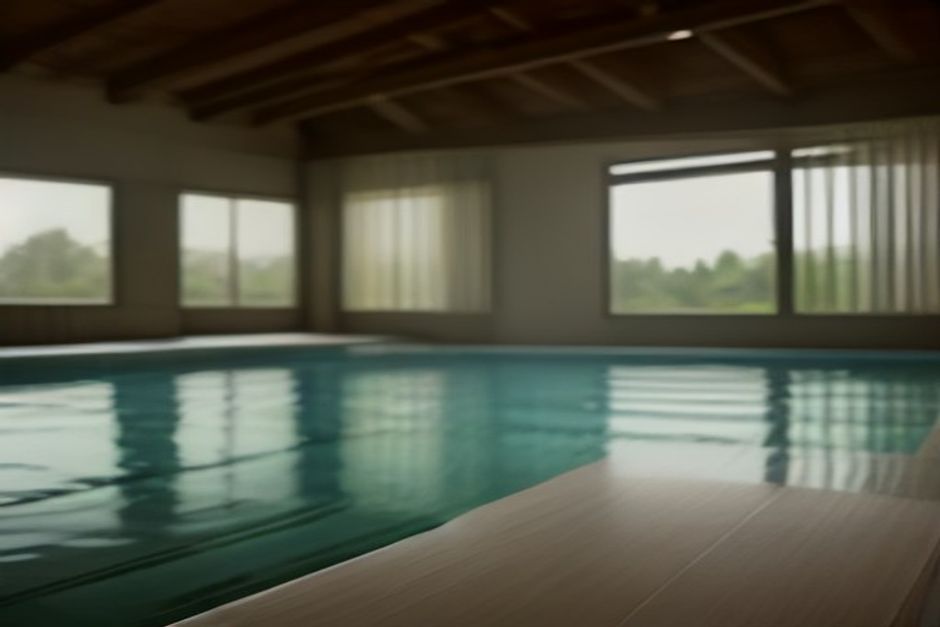 A calm indoor pool lane at sunrise with a rolled yoga mat on a wooden bench at the pool edge