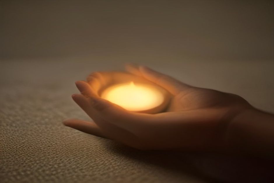 Hands cupped around a small clay candle holder glowing in warm dusk light