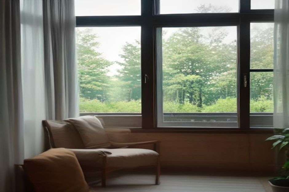 A person seated on a cushion gazing softly out a large window at trees in daylight