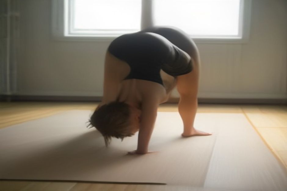 Person in downward-facing dog pose on a mat, spine long with knees slightly bent, bright studio with natural light