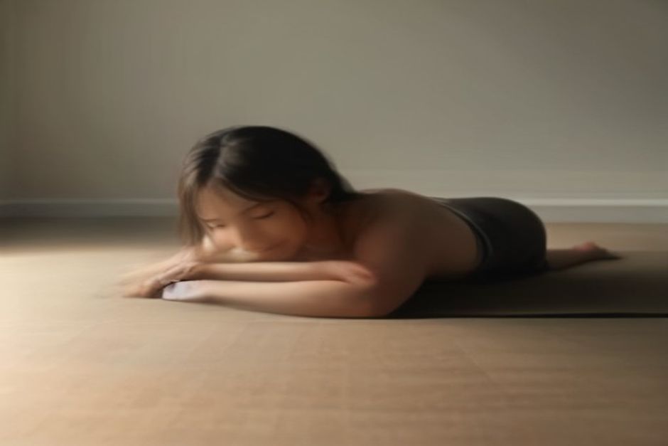 Person lying on their side on a yoga mat in sleeping vishnu pose, head resting on hand, top leg extended upward held by the foot