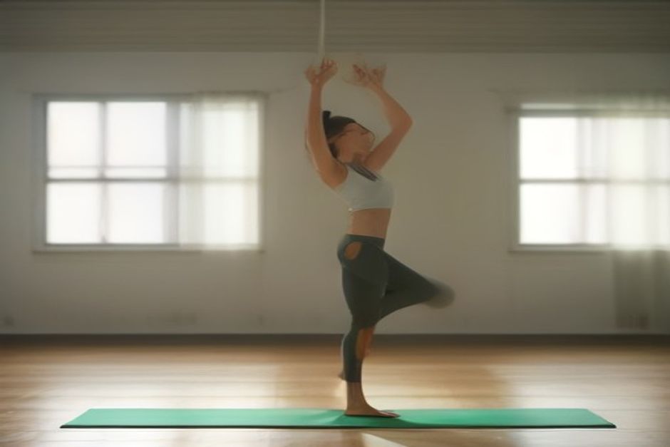 Person standing on a yoga mat in soft morning light, arms swept wide, mid-breath