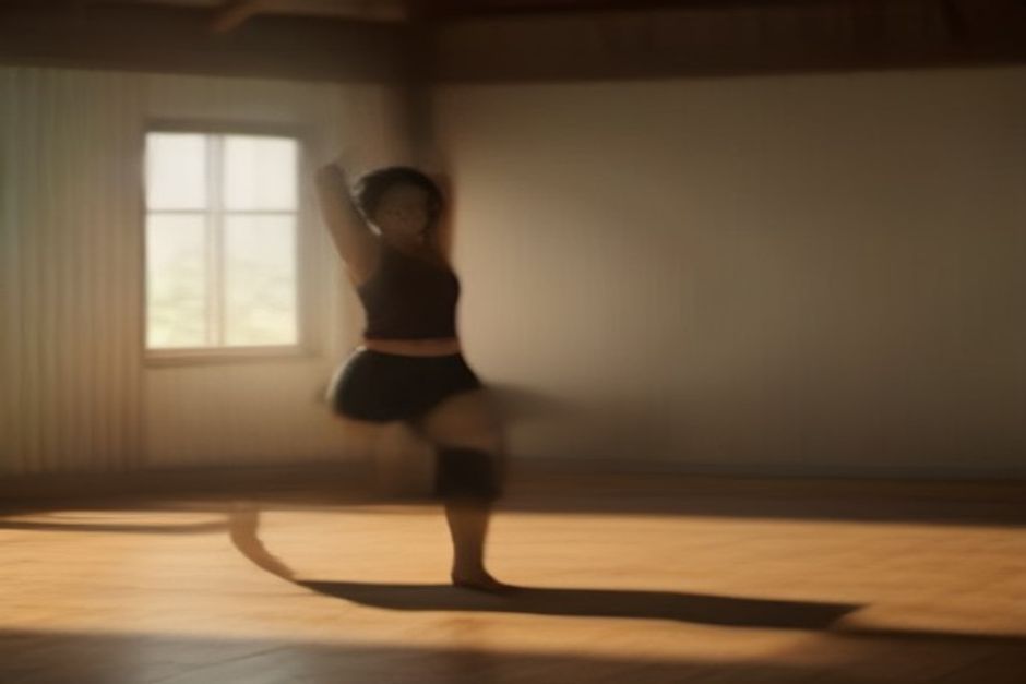 A yoga teacher gently adjusting a student's arms in warrior pose in a warm, wood-floored studio
