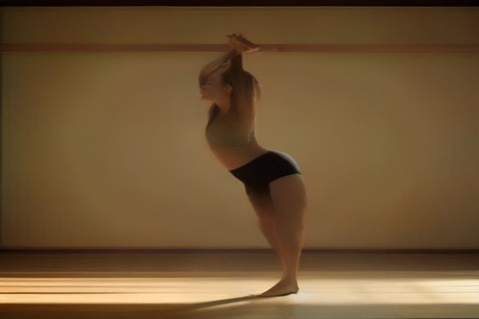 A yoga student in a supported standing pose using a wooden block and strap in a bright, spare studio