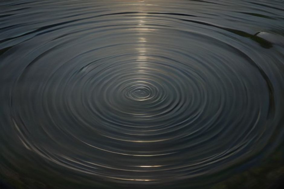 A stone dropping into still water, rings of ripples spreading outward in soft evening light