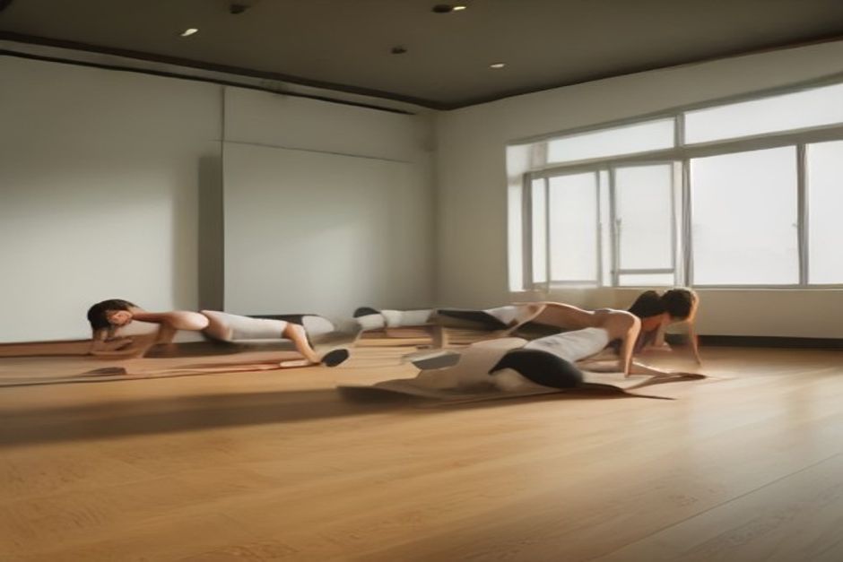 A group of students holding plank pose in a bright modern fitness studio with wooden floors